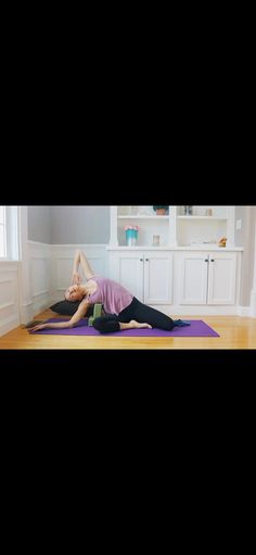 a woman is doing yoga on a mat in the middle of a room with white cabinets