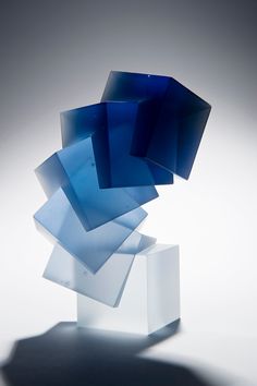 an abstract blue sculpture sitting on top of a white box with shadows coming from it