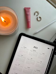 a desk with a calendar, pen and candle on it next to a tablet computer