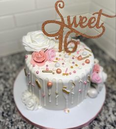 there is a white cake with pink flowers on it and the word sweet 16 spelled in gold