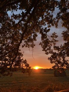 the sun is setting behind some trees in an open field with hay bales on the ground