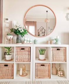 a white shelf with wicker baskets and plants in front of a large round mirror