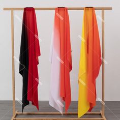 three different colored towels hanging on a wooden rack in front of a white wall and wood floor