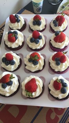 cupcakes with white frosting and strawberries on top are sitting on a tray