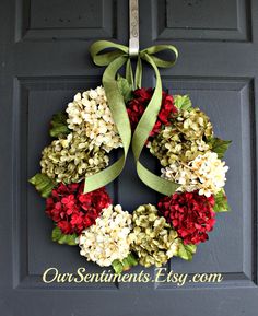 a wreath with red and white flowers is hanging on the front door to welcome guests