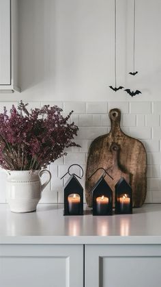 some candles are sitting on a counter next to a cutting board and vase with flowers