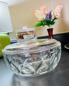 a glass bowl sitting on top of a counter next to a vase with flowers in it