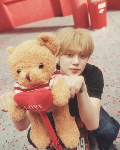 a boy is holding a teddy bear with a red heart on it's chest