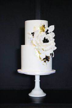 a white and gold wedding cake with flowers on it's tiers, sitting on a black table