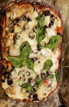 a pizza covered in cheese, olives and spinach on top of tin foil