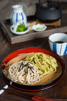 a plate with noodles and chopsticks on a table next to two bowls of soup