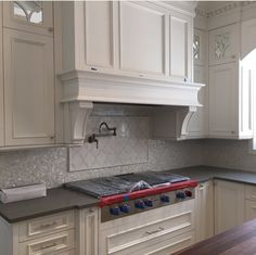 a kitchen with white cabinets and marble counter tops, an oven hood over the stove