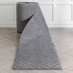 a grey and white rug on the floor next to a gray trash can in an empty room