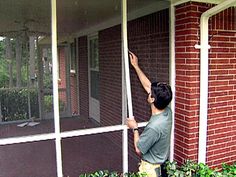 a man standing on the side of a brick building reaching up into a screen door