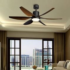 a living room with a ceiling fan in it's center and windows overlooking the city