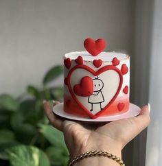 a hand holding a red and white cake with hearts on it