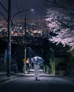 a person holding an umbrella standing on a street at night with the city lights in the background