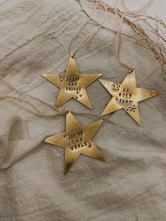 three gold star ornaments with words on them