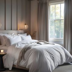 a bed with white sheets and pillows next to a window in a room that has striped walls