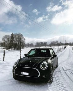 a black car parked in the middle of a snow covered road next to a fence