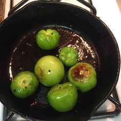 some green apples are cooking in a black pan on the stove top with water running down it