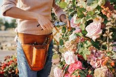 a woman holding a pair of scissors in her right hand while standing next to flowers