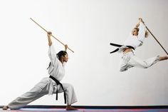 two men doing karate moves with sticks in the air and one man holding on to his leg