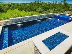 an outdoor swimming pool surrounded by stone walls and blue glass tiles on the sides, with steps leading up to it