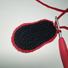 a crocheted black and red object on a white surface with a metal hook