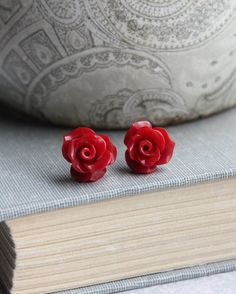 pair of red rose stud earrings sitting on top of a book next to a pillow