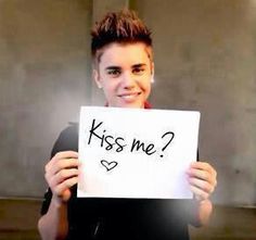 a young man holding up a sign with the words kiss me? written on it