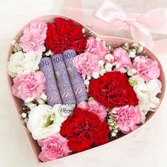 a heart shaped box filled with pink and white carnations, roses and books