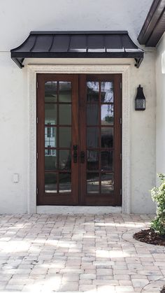 the front entrance to a home with two brown doors and brick pavers flooring