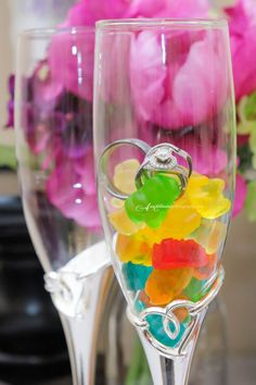 two wine glasses filled with gummy bears on top of a table next to flowers