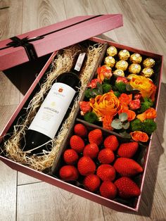 a wine bottle in a box with strawberries and flowers on the floor next to it