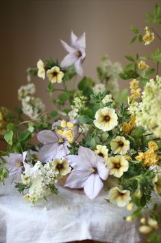 a bunch of flowers sitting on top of a white tablecloth covered table with yellow and purple flowers