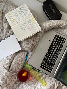 an open laptop computer sitting on top of a bed next to notebooks and pens