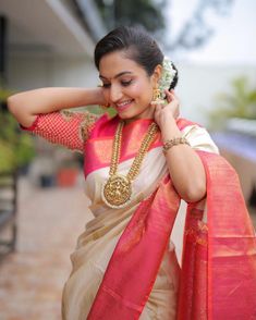 a woman in a white and red sari with gold jewelry on her neck, standing outside