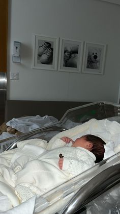 a baby wrapped in a blanket laying on top of a metal bed next to pictures