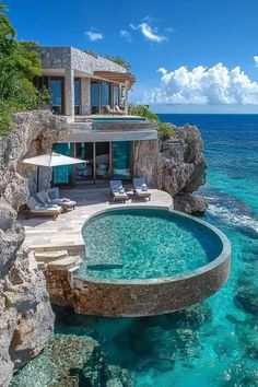 an oceanfront house with a pool and lounge chairs in the water next to it