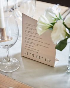 there is a table setting with wine glasses and place cards on it, along with white flowers