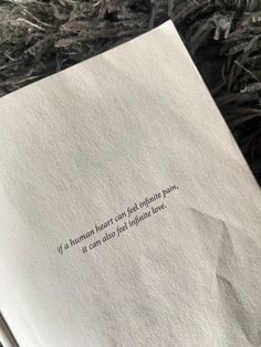 an open book laying on top of a pile of grass next to a tree branch