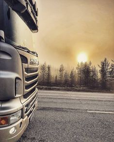 a large truck parked on top of a road next to a forest filled with trees