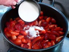 strawberries being stirred with sugar in a pot on the stove top by someone's hand