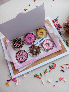 a box filled with assorted donuts sitting on top of a table next to sprinkles