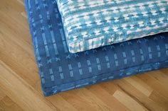 two blue and white pillows sitting on top of a wooden floor next to each other