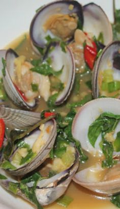 a white plate topped with lots of clams covered in broth and garnish