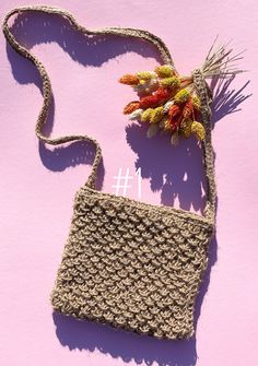 a crocheted purse sitting on top of a pink surface next to a plant