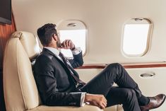 a man in a suit sitting on an airplane seat drinking from a coffee cup and looking out the window