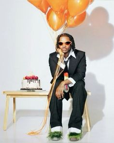 a man sitting in front of a cake and balloons